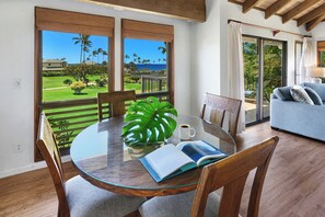 Un coin repas avec une table en verre, des chaises, un livre, une tasse de café et une grande plante tropicale.