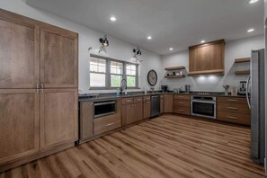 A modern kitchen with wooden cabinets, built-in appliances, and a large window. - Pool | Sleeps 18 | Hot Tub |Firepit | Playset | (Williamstown)