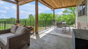 Een overdekt terras met een rieten bank, een tafel en stoelen, met uitzicht op een groen landschap.