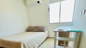 A small, clean room with a bed, a window, a wall-mounted air conditioner, and a white shelf unit. - 3-bedroom apartment in enjoyable Barranquilla with AC for relaxing stays (Barranquilla)