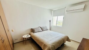 A bedroom with a bed, a small bedside table, a wardrobe, and a window with an air conditioning unit. - 3-bedroom apartment in enjoyable Barranquilla with AC for relaxing stays (Barranquilla)