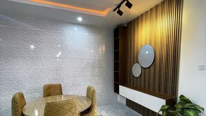 Un comedor moderno con una mesa redonda y sillas acolchadas, un muro con diseño y un panel de madera con estante y adornos.