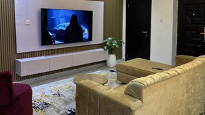 Una sala de estar moderna con un televisor de pantalla plana grande montado en una pared blanca, un sofá color beige, un sillón rojo y una alfombra estampada.