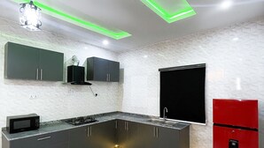 A modern kitchen with dark cabinets, a red refrigerator, and a microwave on the counter. - 2-bedroom apartment in  Ibadan  24/7 light wifi / PS5 (Ibadan)