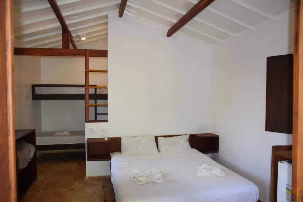 Quarto com beliche, uma cama de solteiro, cabeceiras de madeira e piso ladrilhado.