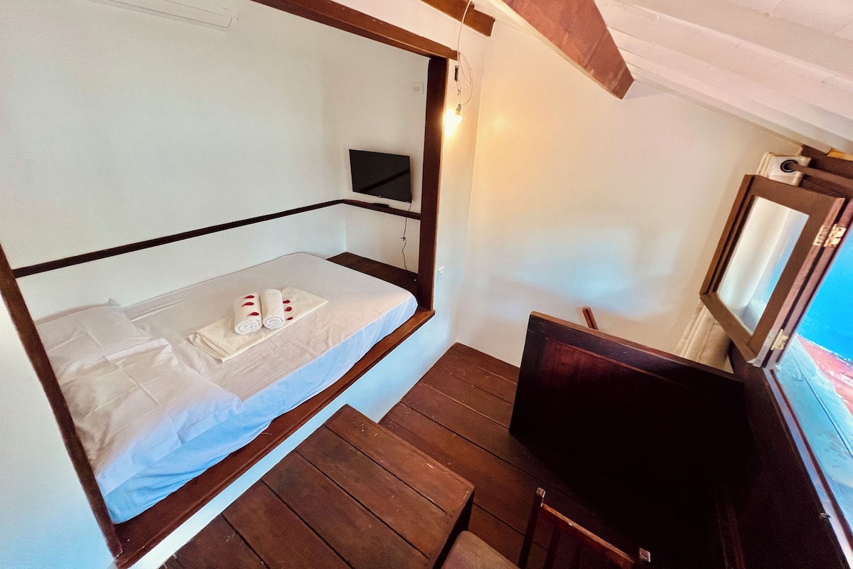 Uma cama beliche com televisão e uma mesa pequena, piso de madeira e janela com vista.
