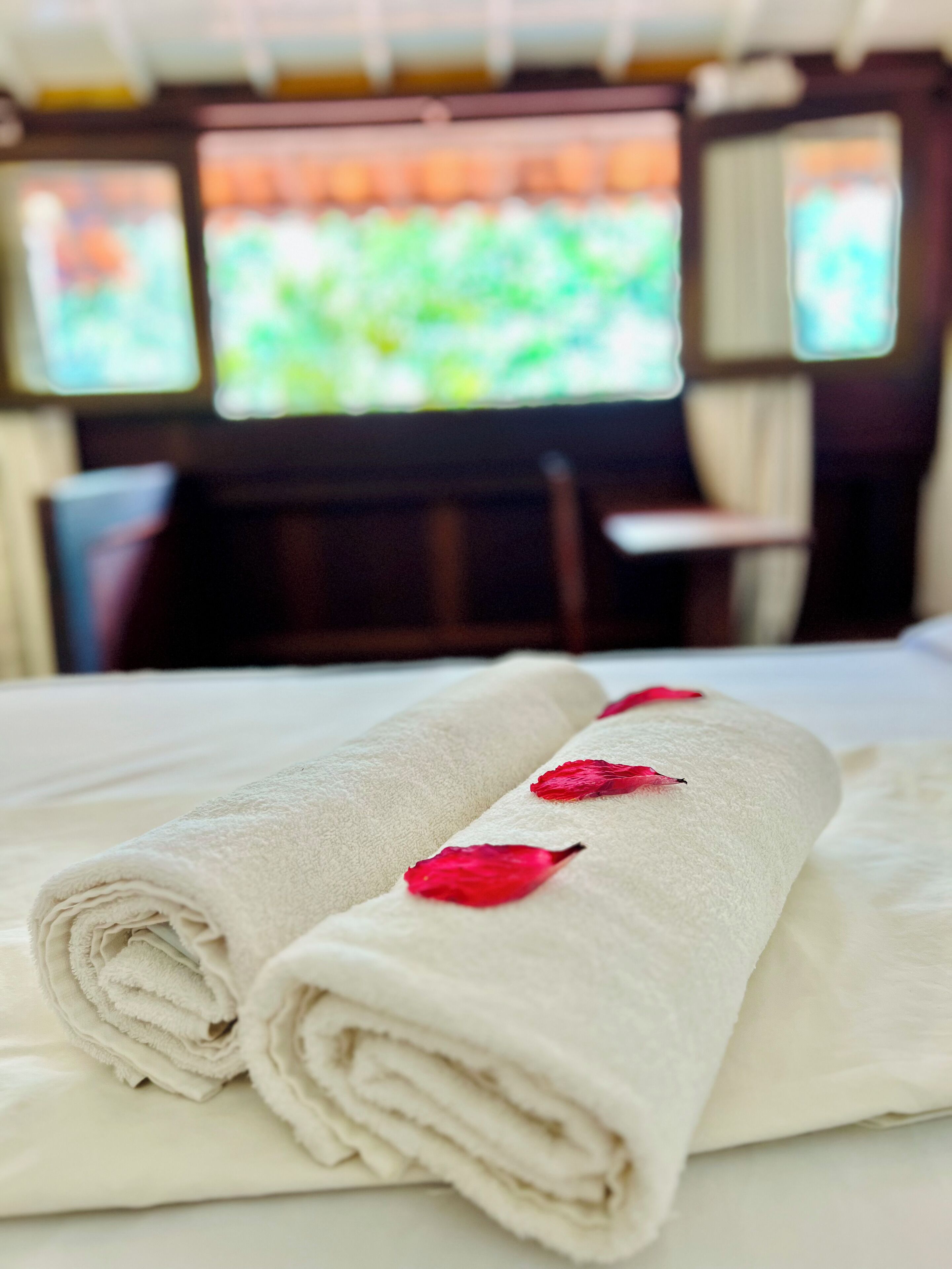 A neatly made bed with rolled white towels and red rose petals placed on them.