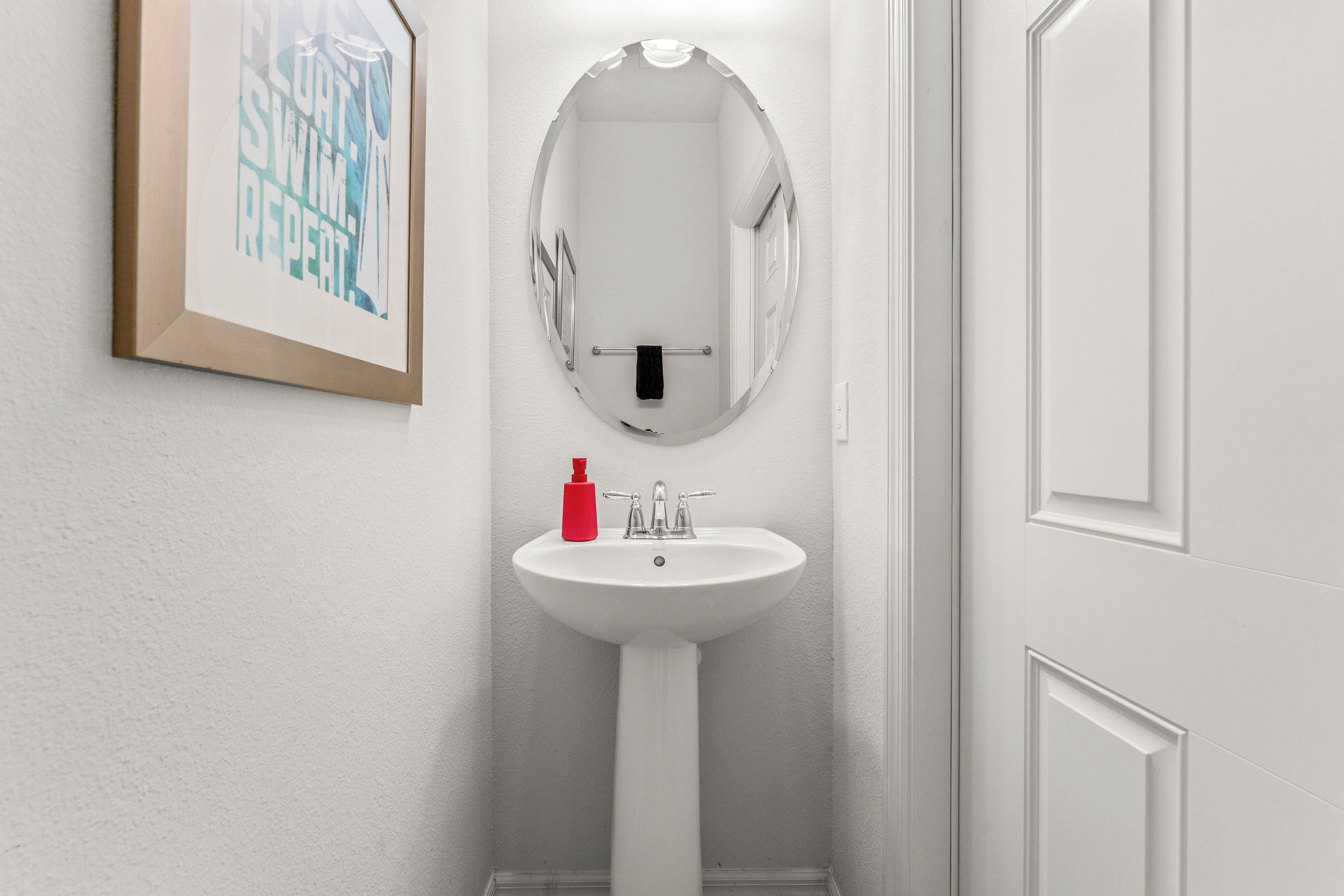 Une salle de bain avec un lavabo blanc, un miroir et une œuvre d’art encadrée au mur.