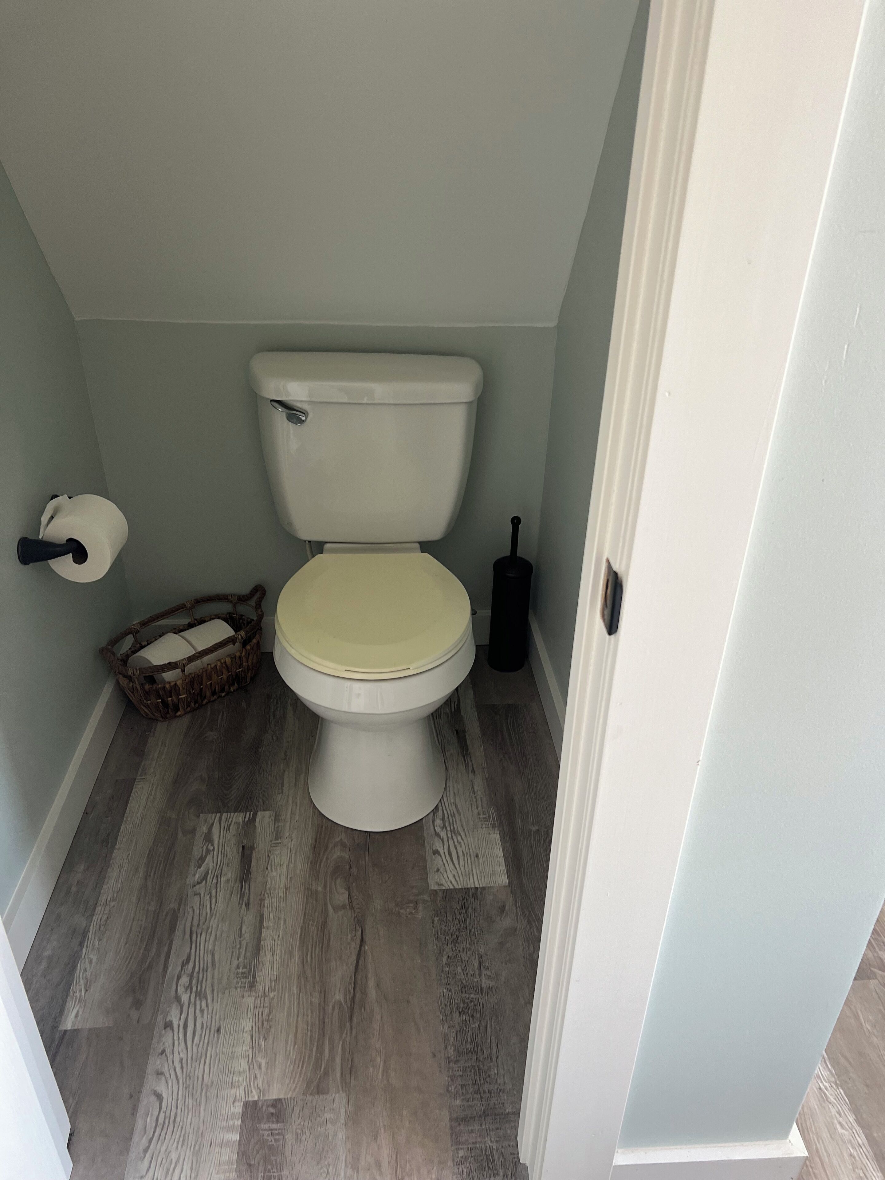 A small bathroom with a toilet, a basket, and a toilet paper roll.