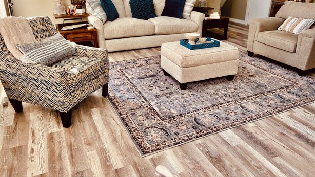 A living room with a sofa, two armchairs, a patterned ottoman, a decorative rug, and a floor lamp.