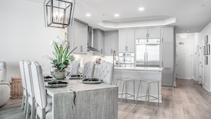 A modern kitchen with grey cabinets, a central island, and stainless steel appliances. - Coastal Three Bedroom Penthouse Offering Breathtaking Bayside Views. Complimentary Boat Slip! (Orange Beach)
