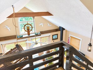 A high-ceilinged room with a wooden ceiling, a ceiling fan, and a window with a view of greenery.