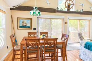 A dining area with a wooden table and chairs, a ship-themed painting, and a ship's wheel decoration. - Perfect 2-bedroom Big Long Lake Cottage (Wolcottville)