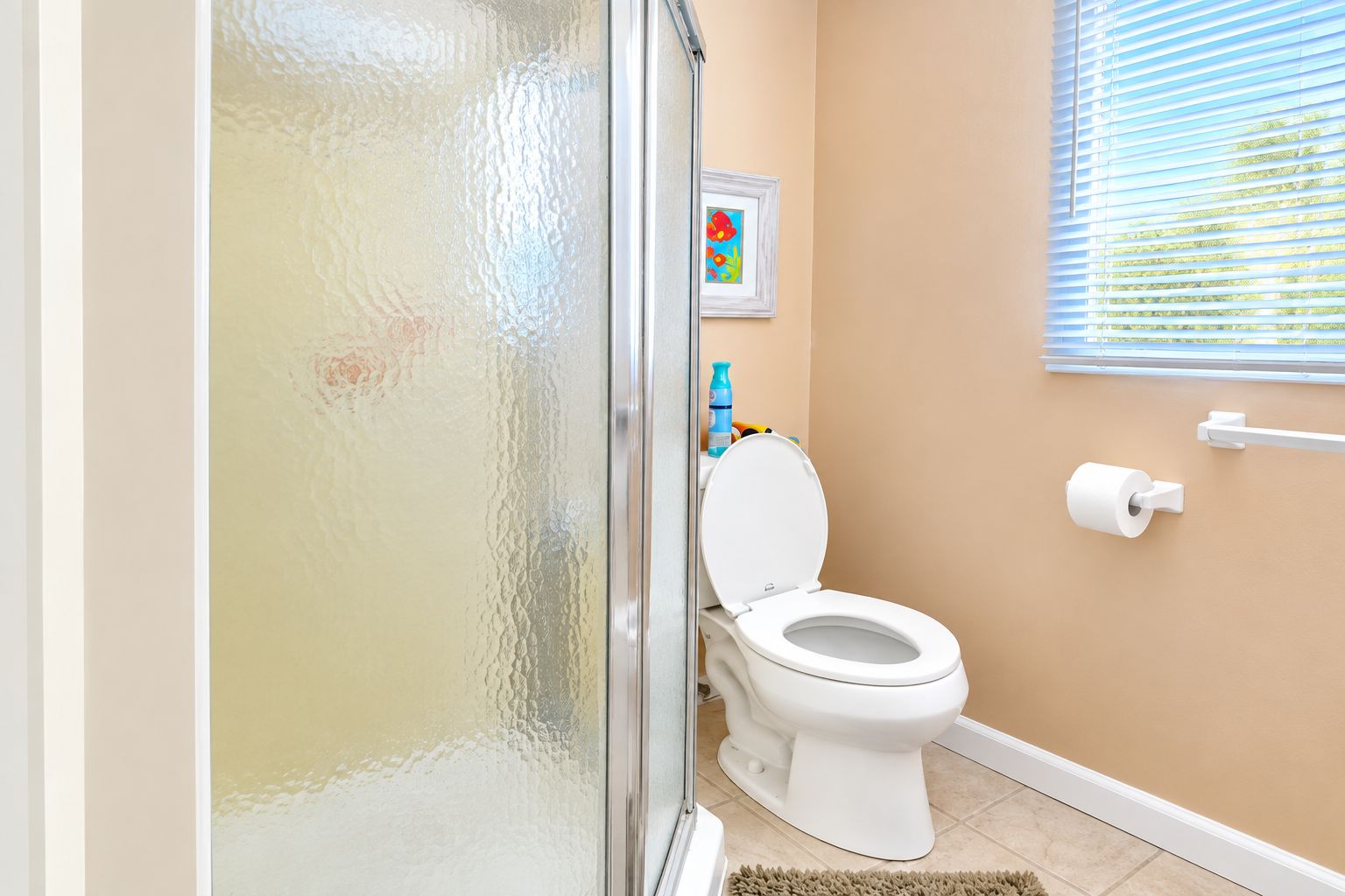 A bathroom with a toilet, a shower, a towel rack, and a window with blinds.