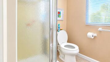 A bathroom with a toilet, a shower, a towel rack, and a window with blinds.