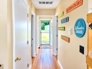 A hallway with wooden flooring leading to a door, decorated with motivational signs and a saltwater sunshine sign. - Perfect 2-bedroom Big Long Lake Cottage (Wolcottville)