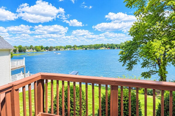 A deck with a view of a lake, surrounded by greenery and houses.
