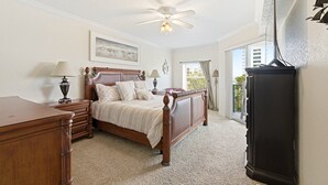 A bedroom with a wooden bed, a nightstand, a dresser, a ceiling fan, and a view of the outdoors. - Oceanwalk 3BR | Ocean Views, Private Balcony & Steps to Car-Free Beach (New Smyrna Beach)