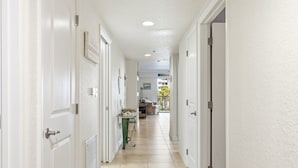 A hallway with white walls, a tiled floor, and doors leading to other rooms. - Oceanwalk 3BR | Ocean Views, Private Balcony & Steps to Car-Free Beach (New Smyrna Beach)