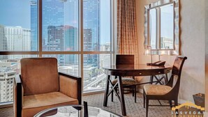 A hotel room with a large window, a round table, a chair, a lamp, and a mirror. - MGM Signature- F1 & Strip View Jacuzzi Balcony (Las Vegas)