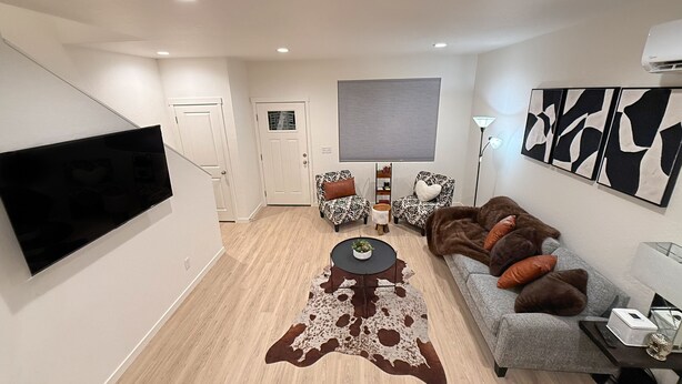 Una sala moderna con un televisor de pantalla plana, dos sillones estampados, un sofá gris, un tapete de cuero de vaca y arte abstracto en la pared.
