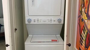 Eine kompakte, weiße Waschmaschine und Trockner-Kombination mit Bedienfeld in einem schmalen Raum mit Fliesenboden.