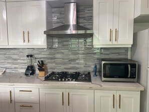 A modern kitchen with white cabinets, a stainless steel range hood, a gas stove, a blender, a knife block, and a microwave. - Oceanfront 2-bedroom 1st floor condo in serene Cabarete with AC & pool (Cabarete)