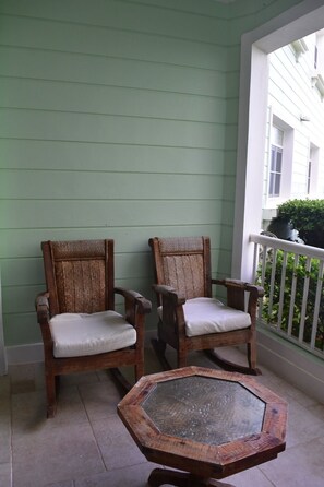 Zwei Holzstühle mit weißen Kissen auf einer Veranda mit einem sechseckigen Holztisch.