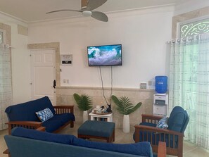 A living room with a television mounted on the wall, a ceiling fan, and a water dispenser. - Oceanfront 2-bedroom 1st floor condo in serene Cabarete with AC & pool (Cabarete)