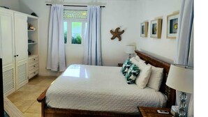 Ein Schlafzimmer mit Bett, Deckenventilator, Fenster mit Vorhängen, einer Dekoration mit Seestern und gerahmten Bildern an der Wand.