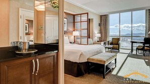 Habitación de hotel con cama, mesita de noche, lámpara, silla y un amplio ventanal con vistas.