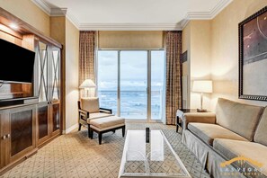 Habitación de hotel con un ventanal que ofrece vista al océano, un televisor de pantalla plana, un sofá, una silla y una mesa de centro.