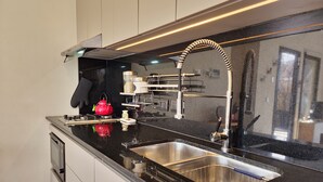 Une cuisine moderne dotée d’un évier en acier inoxydable, d’un plan de travail noir et d’une bouilloire rouge.