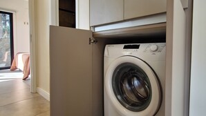 Une petite buanderie équipée d’un lave-linge à chargement frontal, d’un meuble de rangement au-dessus et d’une porte donnant sur un balcon.