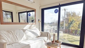 Un salon avec un canapé blanc, un petit tabouret en bois et une grande fenêtre donnant sur l’extérieur.