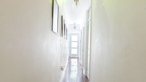 A long, narrow hallway with white walls and wooden floors, leading to a bright room at the end.