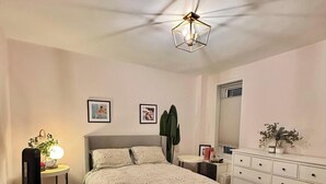 A bedroom with a bed, bedside tables, a dresser, a ceiling light fixture, and a large mirror.