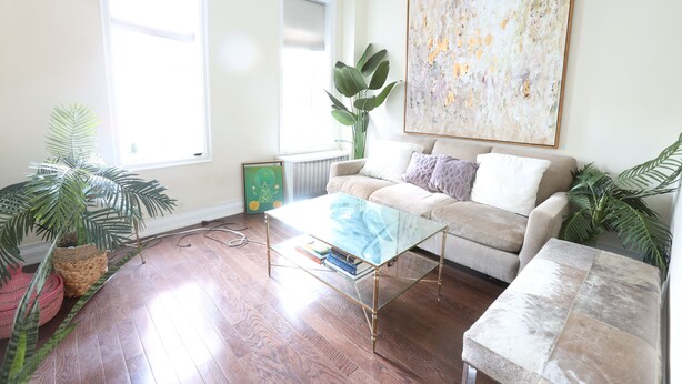 A living room with a glass coffee table, a beige sofa, and a large abstract painting on the wall.