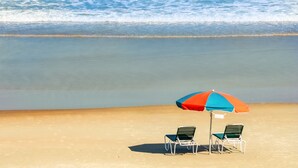 Ein Strand mit zwei Stühlen und einem bunten Sonnenschirm.