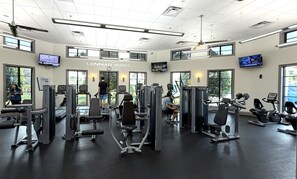 Ein Fitnessstudio mit verschiedenen Trainingsgeräten, großen Fenstern und einem Schild mit der Aufschrift 'LENNAR HOMES'.