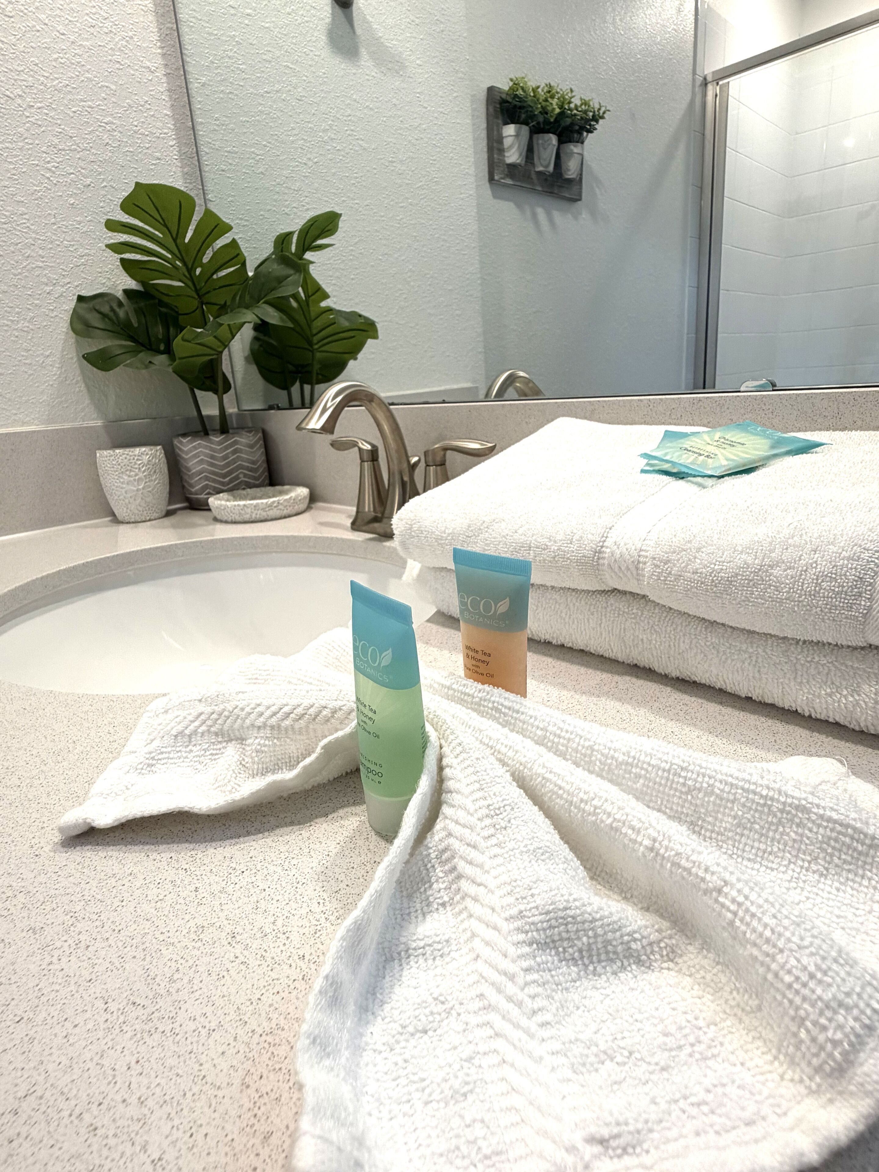 A bathroom with a sink, two potted plants, a mirror, and towels.