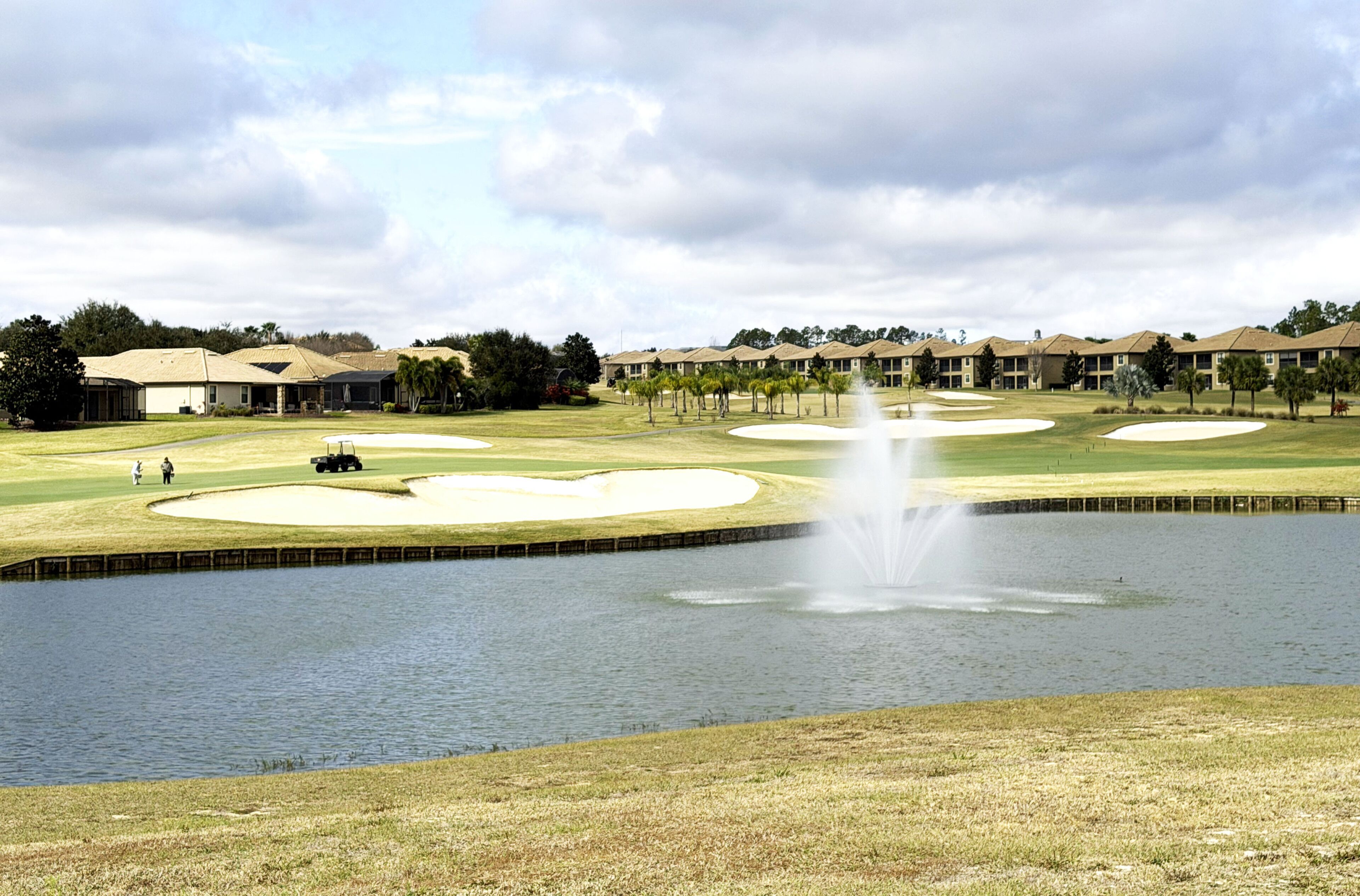 Un campo da golf con bunker, uno stagno e una fontana.