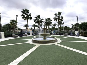 Ein Brunnen im Zentrum einer begrünten Anlage mit Kunstgrashalm.