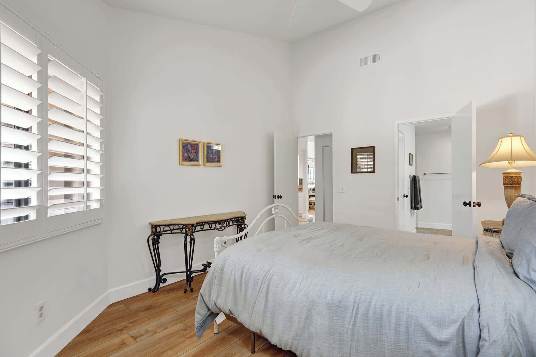 A bedroom with a bed, a bedside table, a mirror, and a window with blinds.