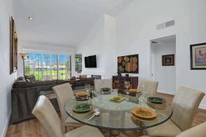 A dining area with a glass table and chairs, surrounded by white walls and a large window. - Gorgeous fairway views|Pet-friendly|Club access (Palm Desert)