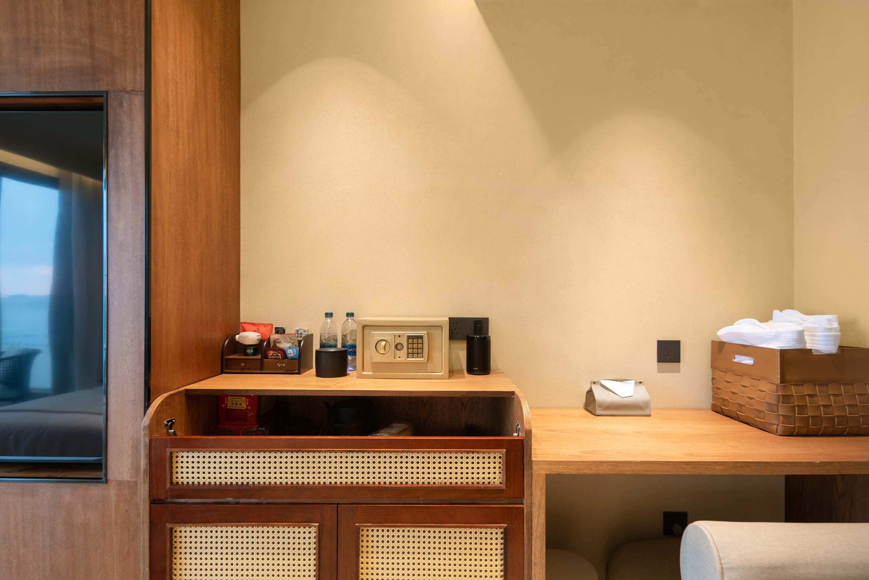 A hotel room with a wooden desk, a radio, a telephone, and a basket of towels.