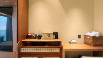 A hotel room with a wooden desk, a radio, a telephone, and a basket of towels.