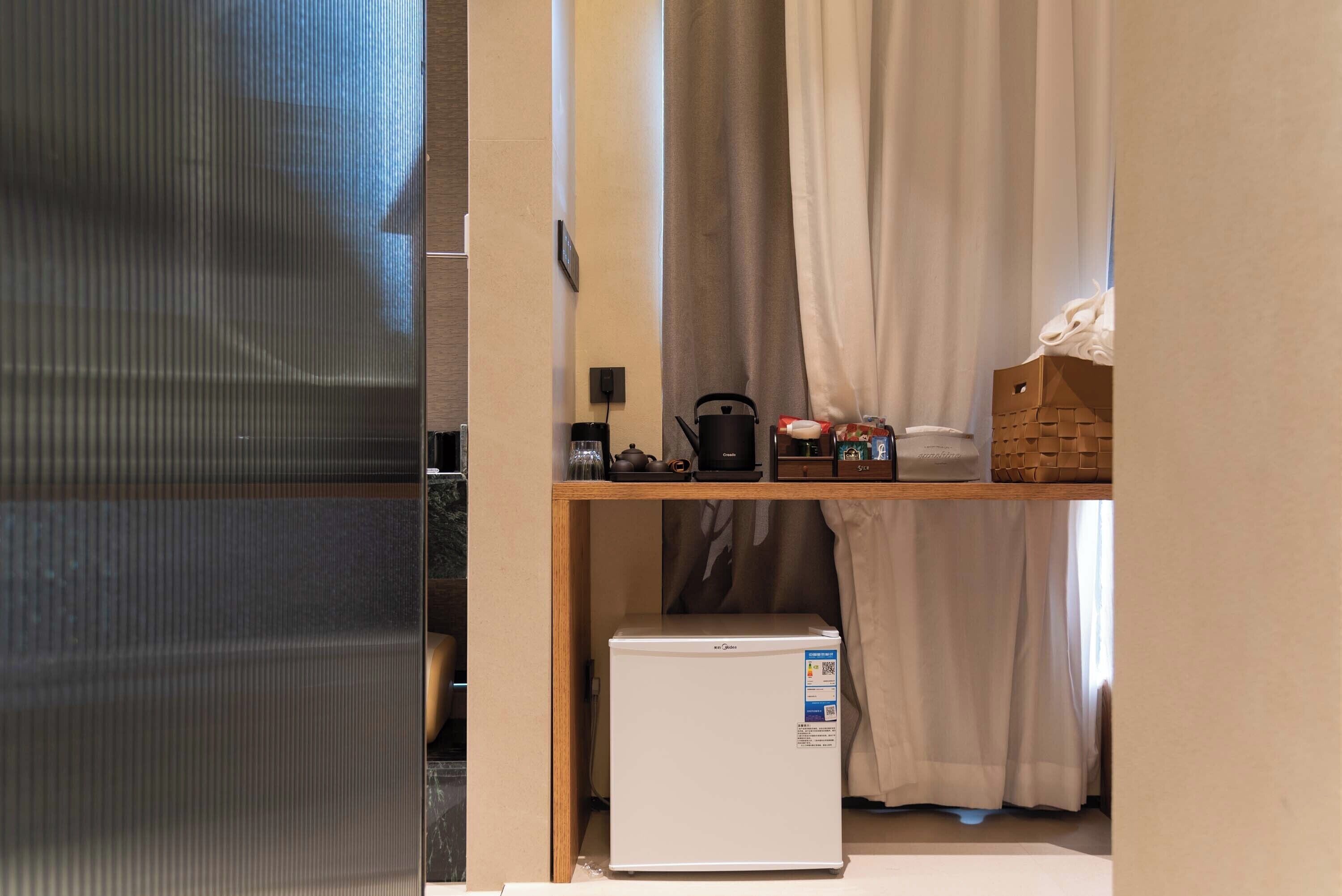 Una cuina petita amb un frigorífic blanc, una estant de fusta amb utensilis de cuina i un armariet.