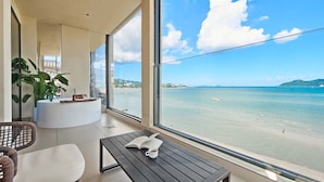 A modern room with a large window overlooking a beach, a round white table, a wicker chair, and a potted plant. - Santa Monica Seaview Vacation Home (Shenzhen)