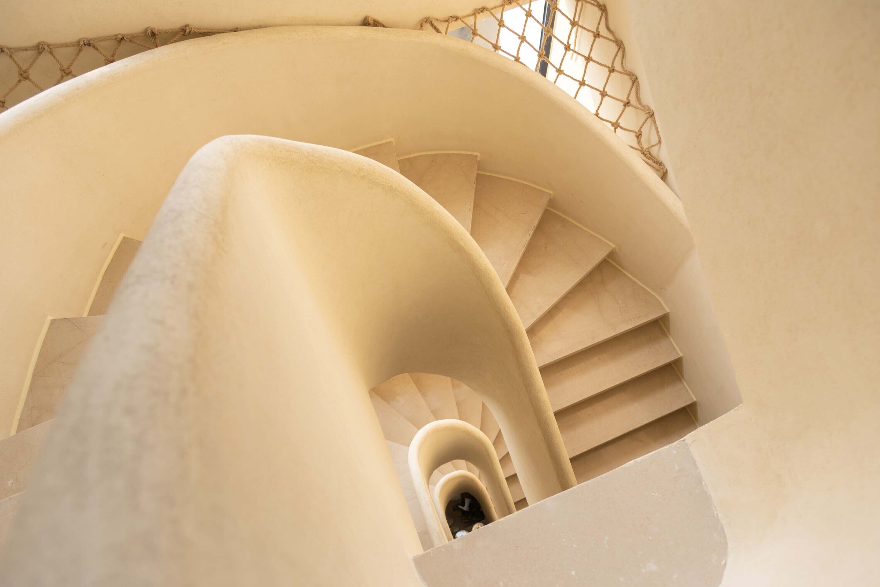 Una escalera en espiral con una decoración color beige y barandilla de malla metálica.